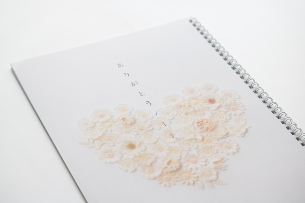 写真。ありがとうノートの表紙が写っている。優しい色合いの和紙の花がハート型に並べられてあしらわれている。